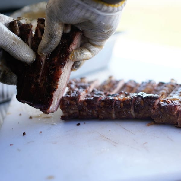 Gloved hands separating a rack of Rack City Ribz BBQ ribs on a white cutting board.