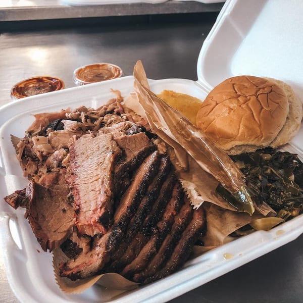 Rack City Ribz BBQ platter with sliced brisket, pulled pork, collard greens, bun, and sauces.