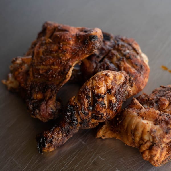 Close-up of Rack City Ribz BBQ chicken pieces with crispy, charred skin on a metal surface.