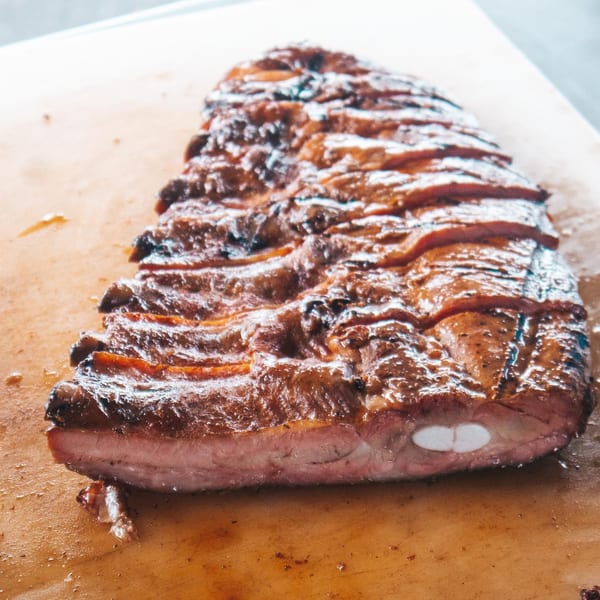 Rack City Ribz's glistening, perfectly cooked BBQ ribs, sliced and ready to serve on a wooden board.