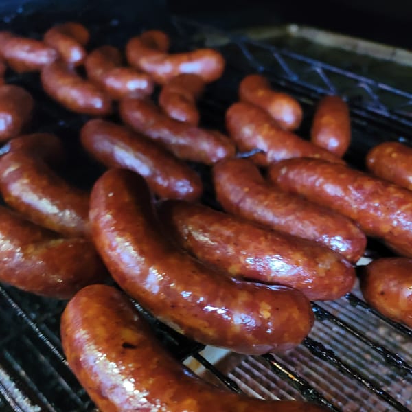 Sausages with a glossy, reddish-brown skin cooking on a dark grill grate.