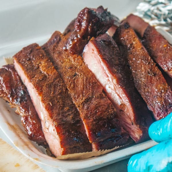 Close-up of Rack City Ribz's BBQ ribs, glistening with sauce, served in a white container.